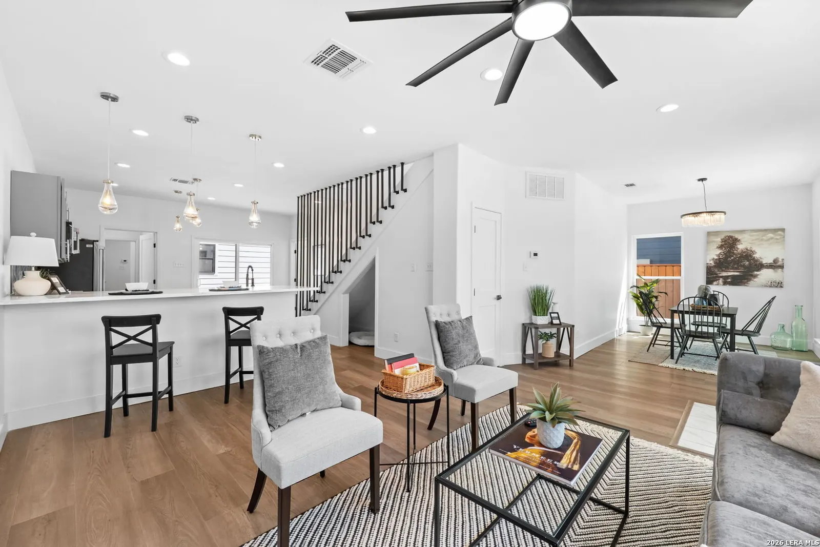 Open concept living room staged near stairs and kitchen bar seating